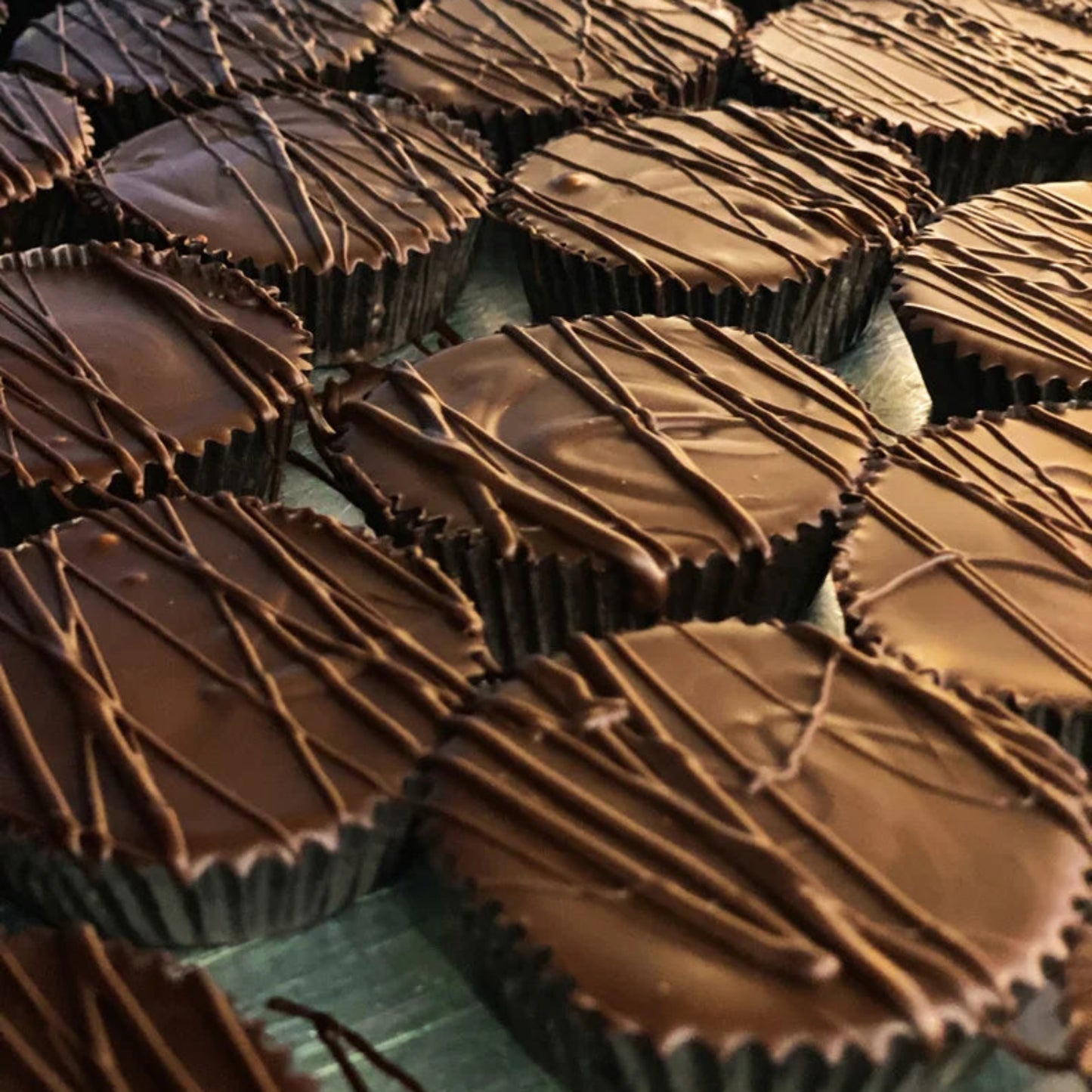 Close-up of multiple chocolate cups with a drizzled topping on a green surface.