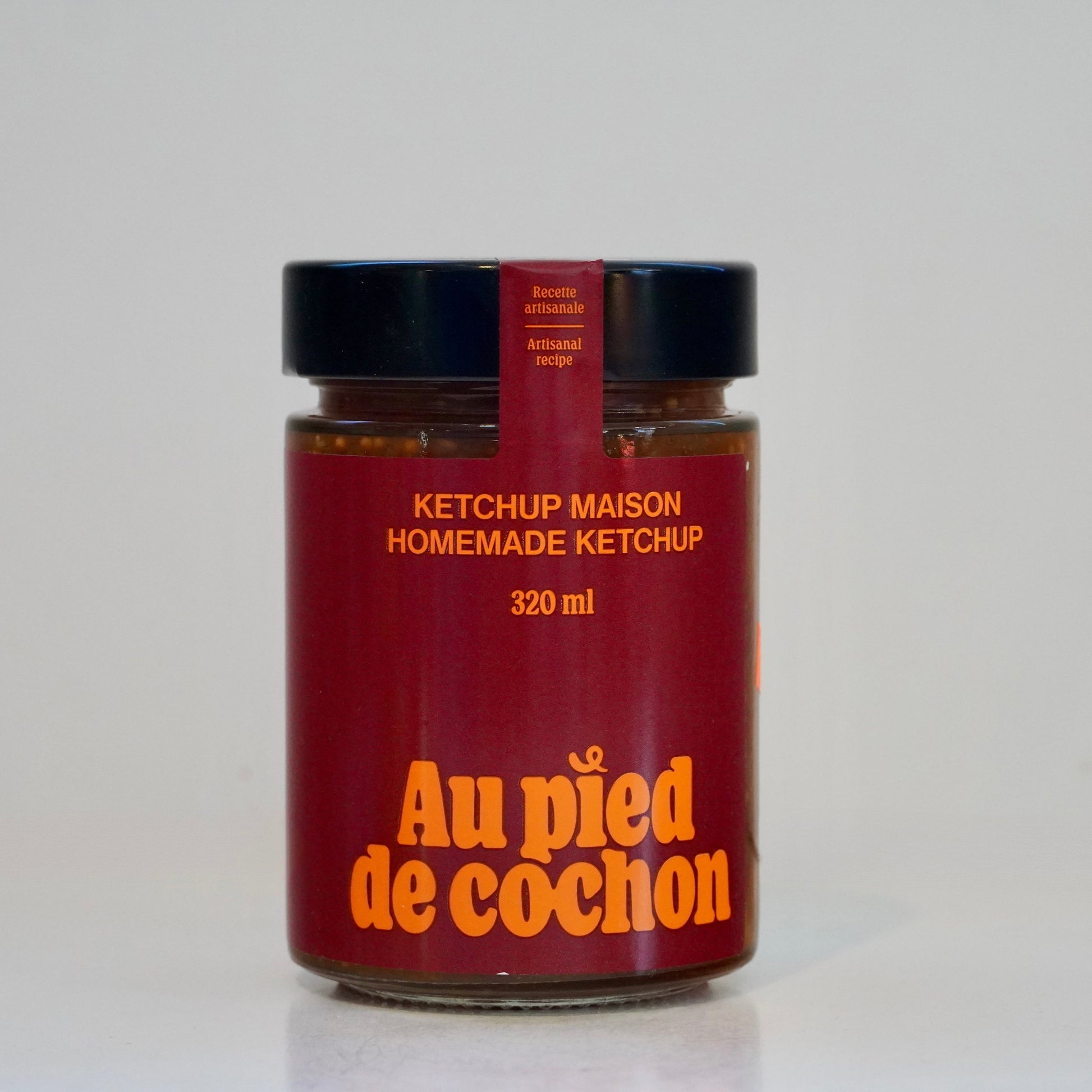 Jar of homemade ketchup with red label and black lid on a white background