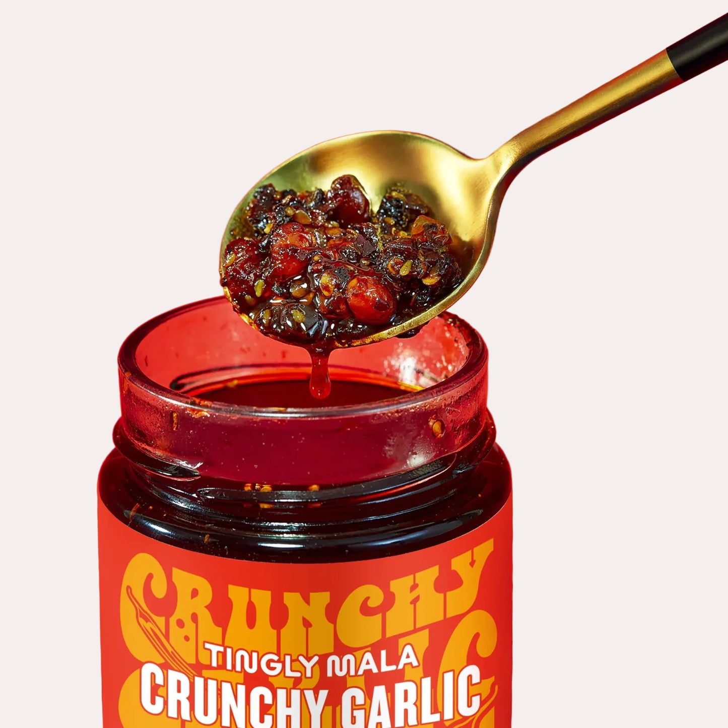 Jar of 'Crunchy Tingly Mala Crunchy Garlic' with a spoonful of spicy condiment on a red background