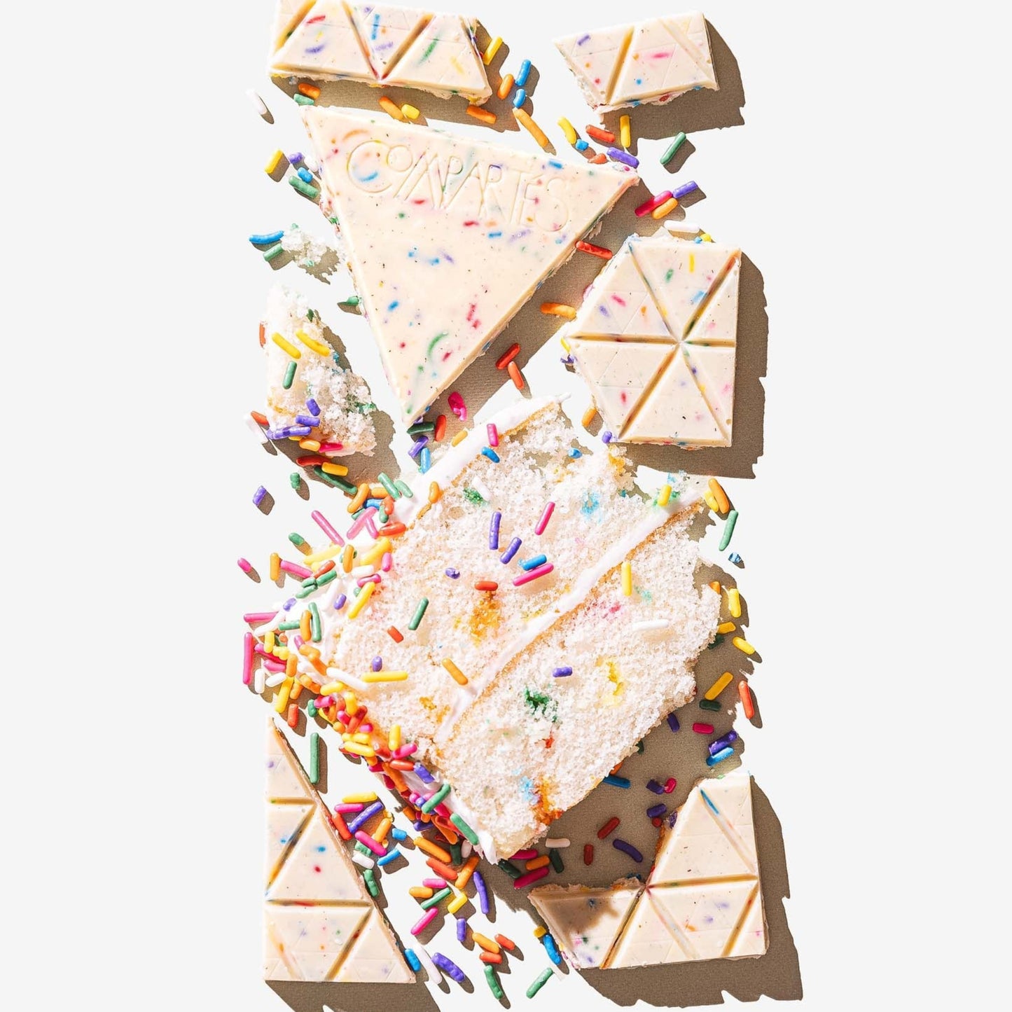 Triangular pieces of cake with white frosting and colorful sprinkles on a white background