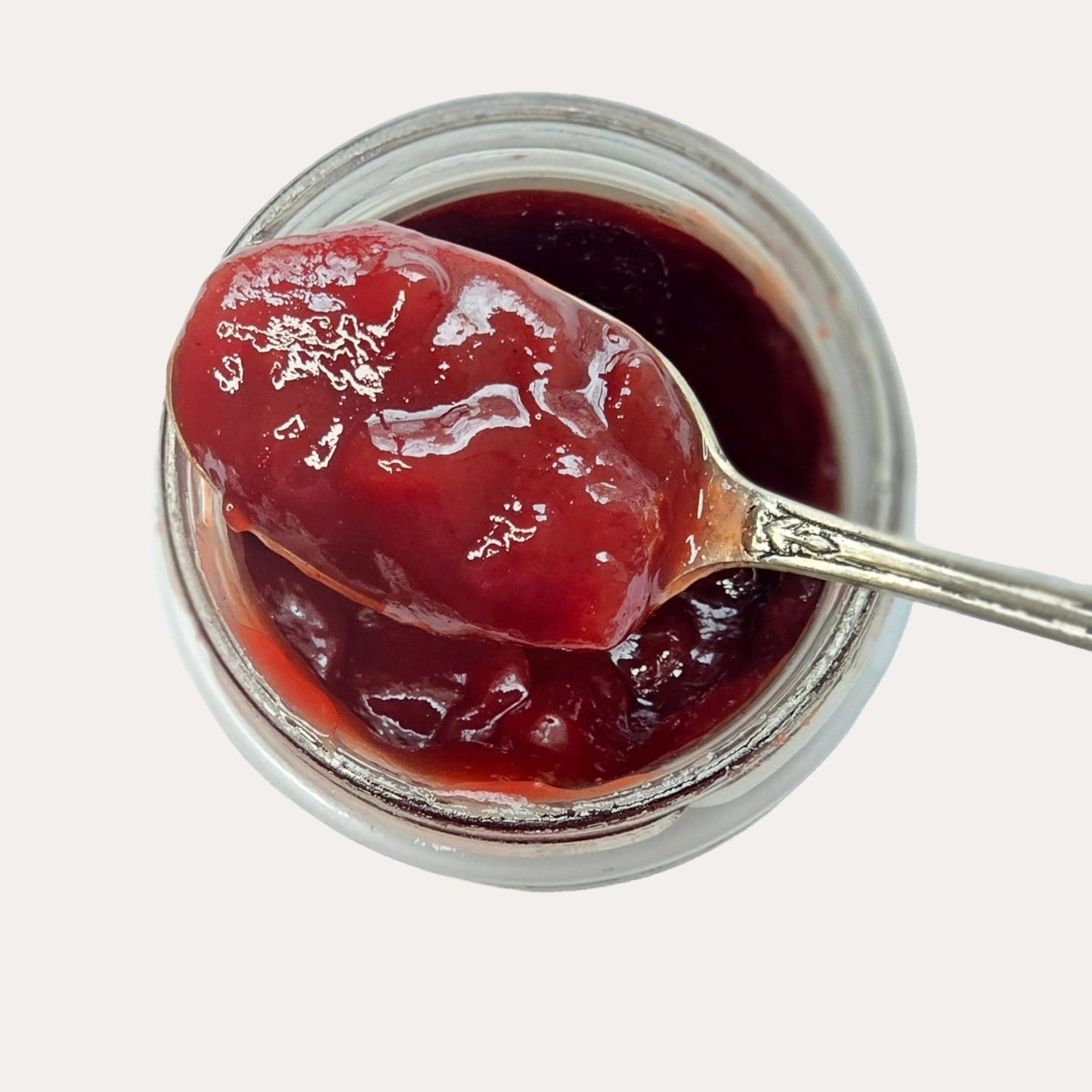 Jar of red jelly with a spoonful being lifted, on a light gray background