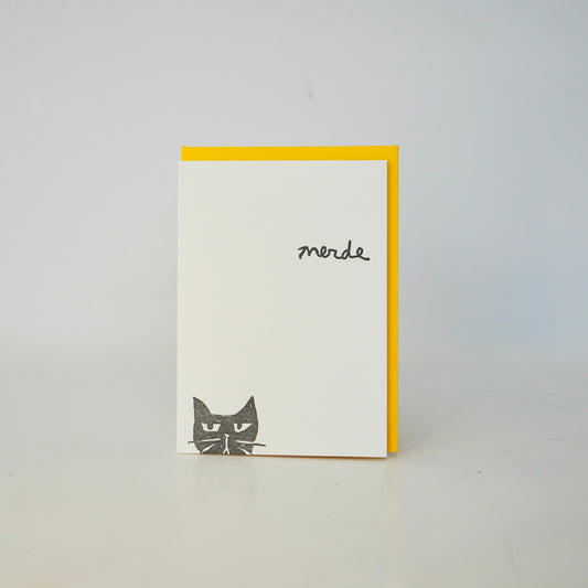 Card with a black cat illustration and 'merde' text on a white background