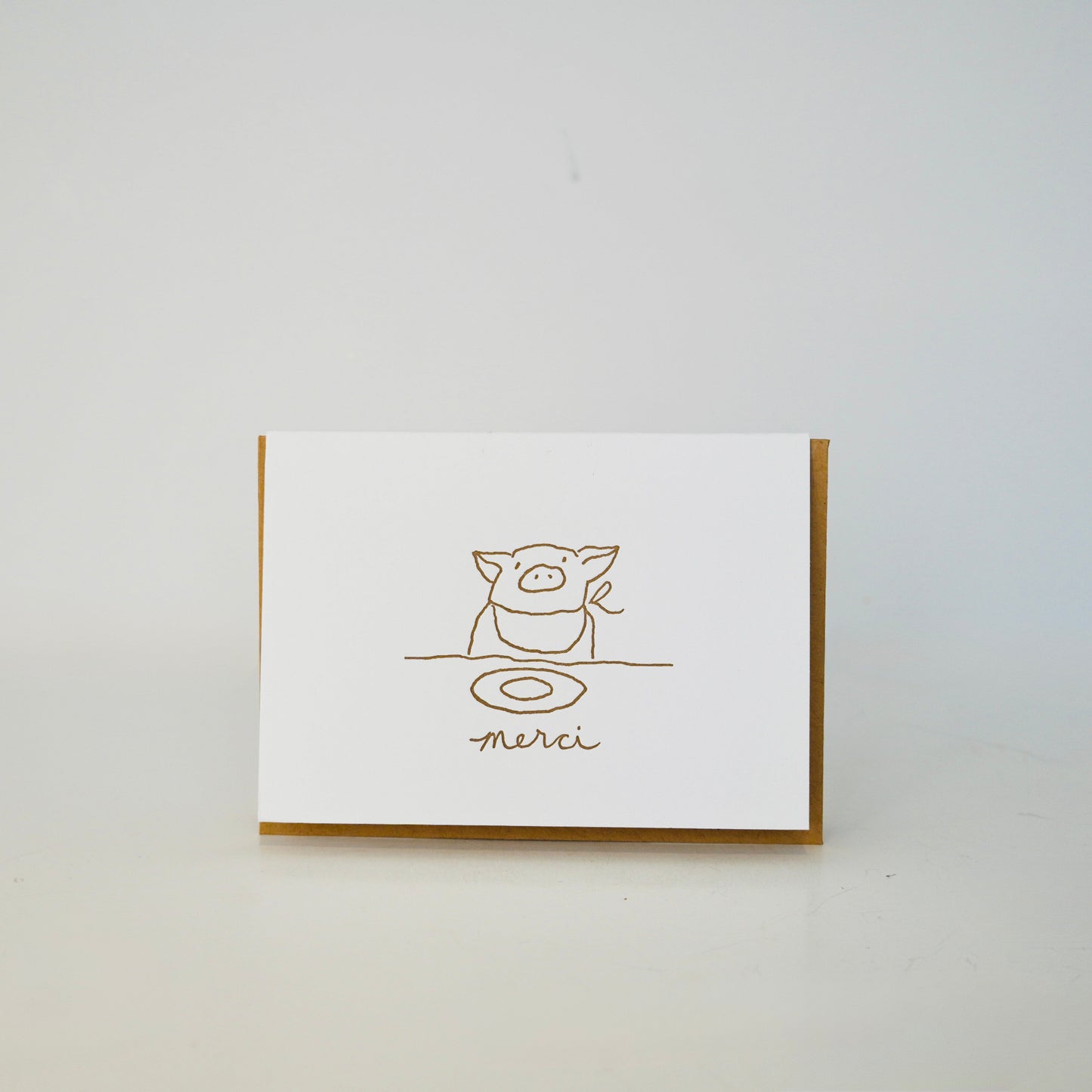 White card with gold line art and 'merci' text on a white background