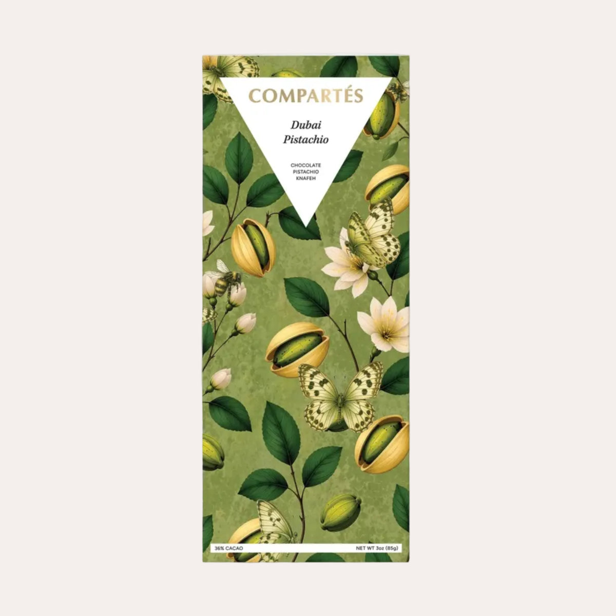A Compétés chocolate bar in a tall rectangular wrapper featuring a botanical illustration pattern of green leaves, white flowers, and pistachios on a muted olive-green background. The brand name 'COMPÉTÉS' is printed in gold at the top, and 'Dubai Pistachio' is written in the center.