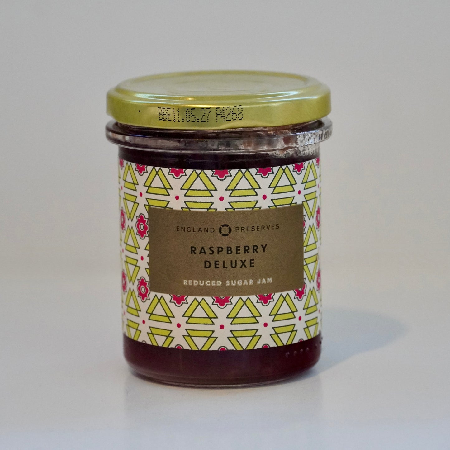 Jar of raspberry preserve with decorative label on a white background