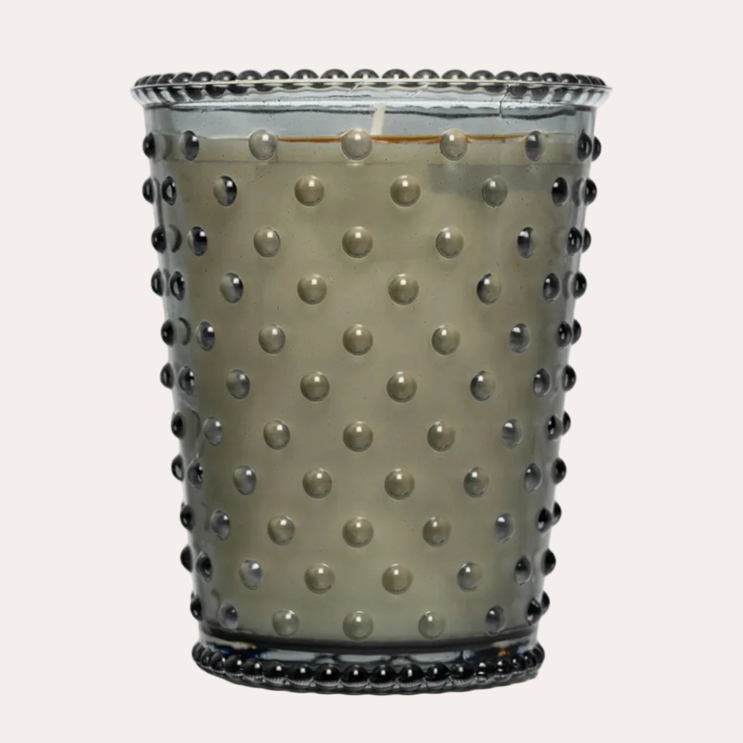 A Hobbit candle in a smoky gray hobnail glass jar with a beaded rim and base, featuring a textured gray wax insert.