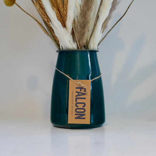Teal vase with dried plants on a white surface and light gray background