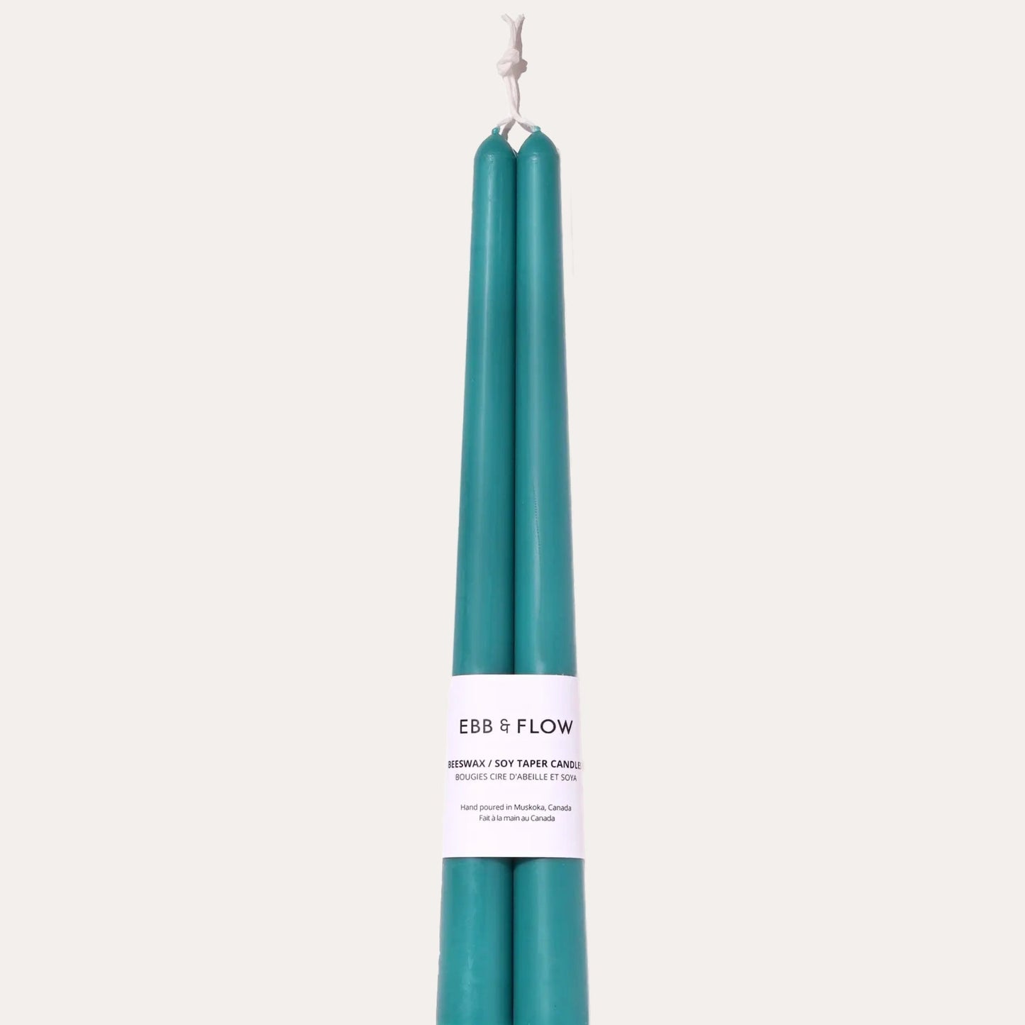 Two teal candles with a white label on a light beige background