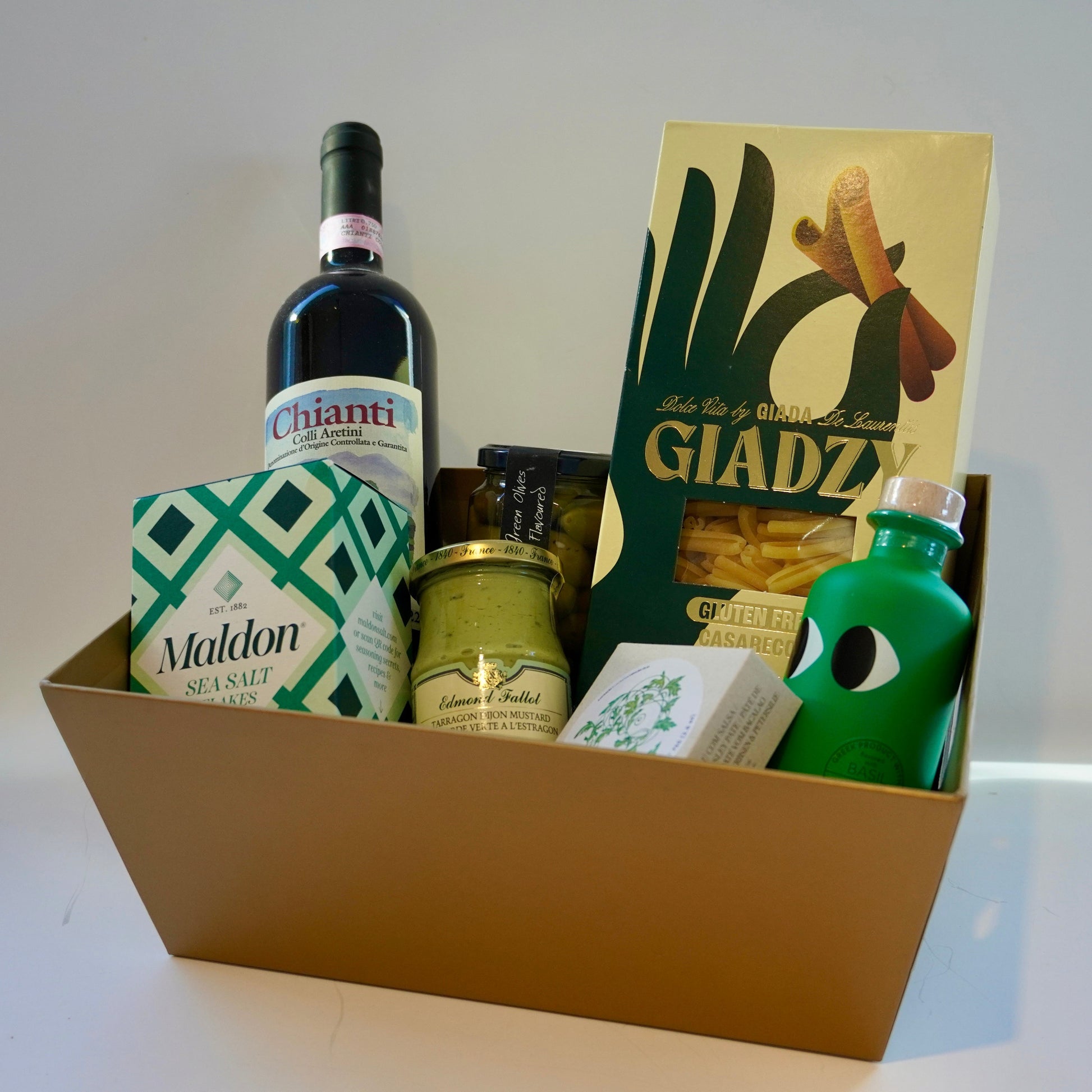 Gift basket with Chianti bottle, pasta, olive oil, and other items on a white surface.