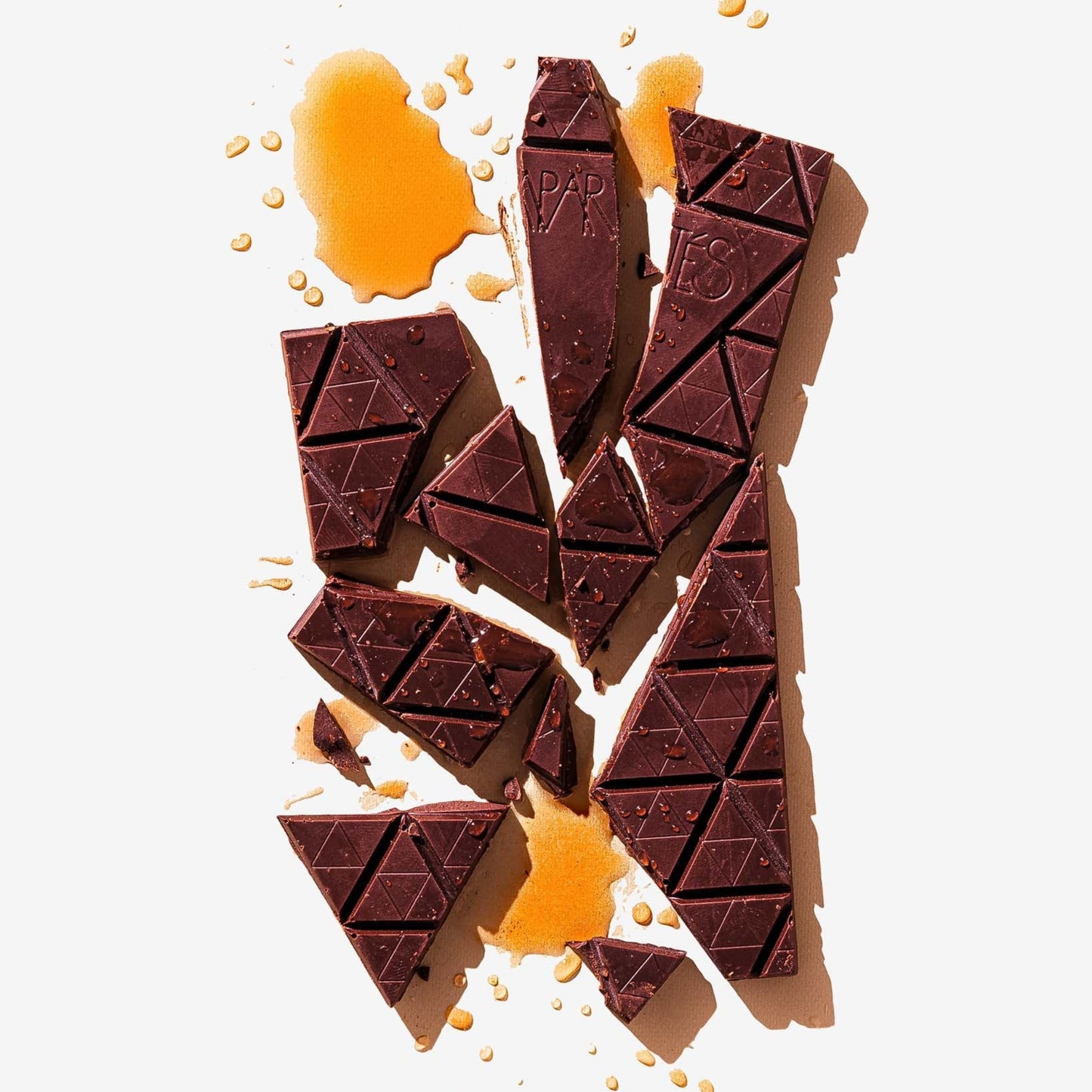 Dark chocolate bars with a splash of orange liquid on a white background