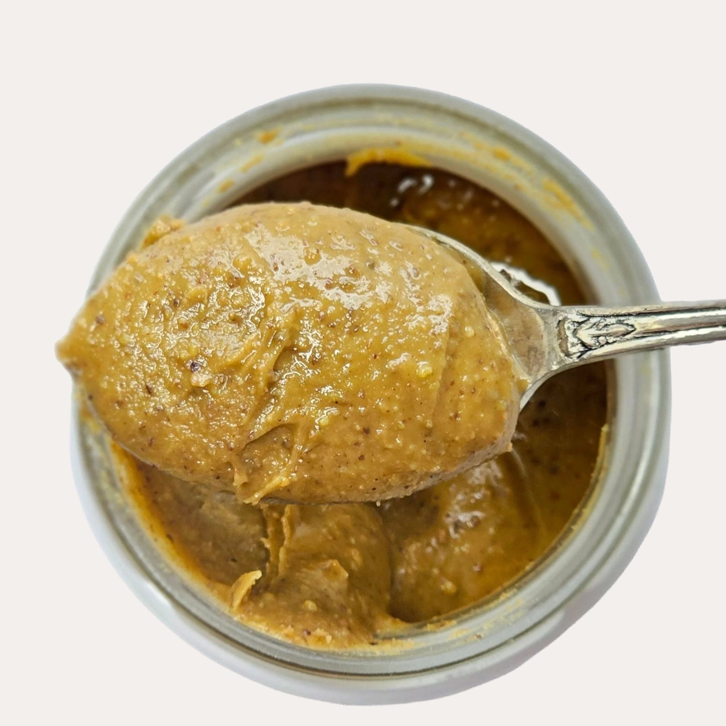 Jar of pistachio spread with a spoonful being lifted out, on a white background