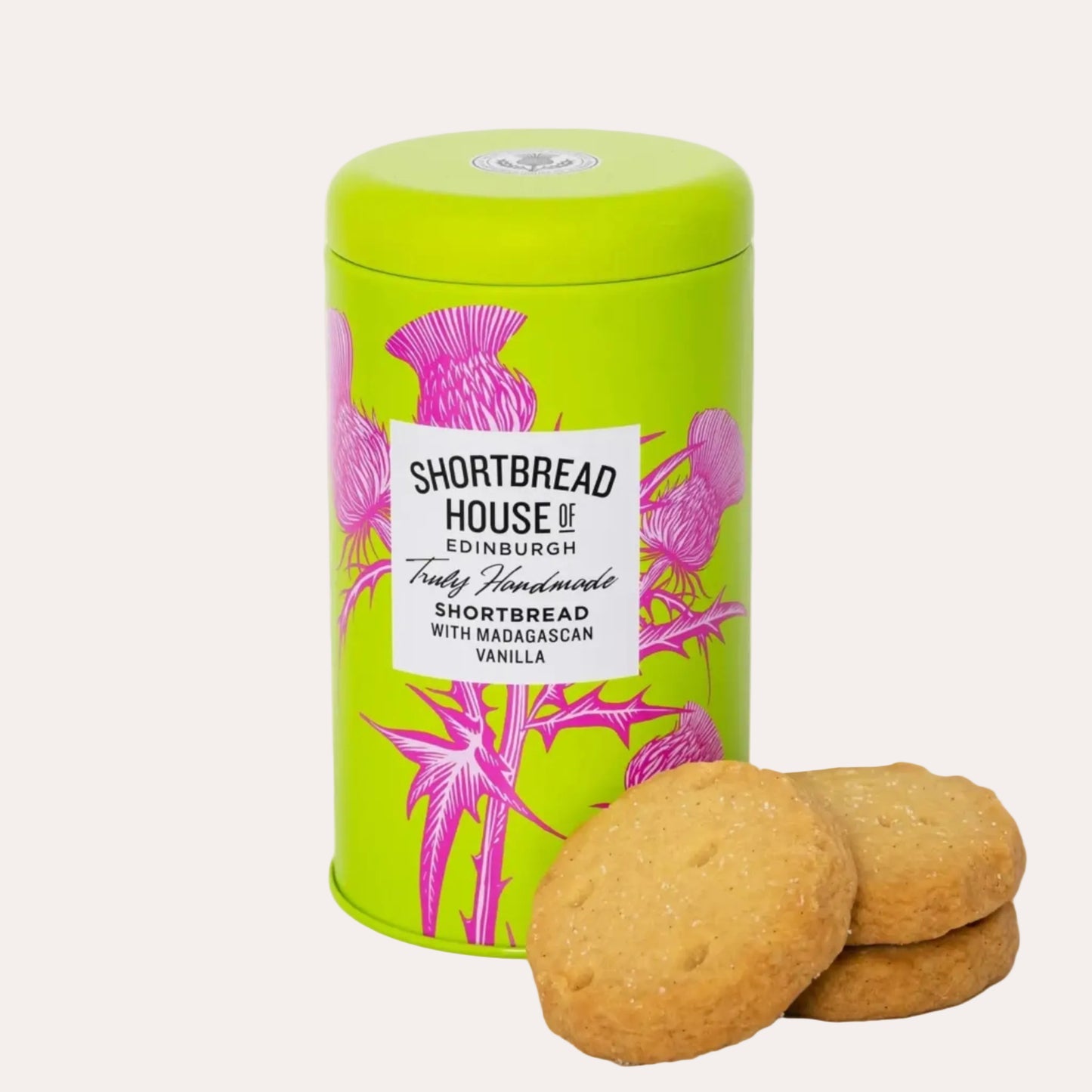 Green cylindrical cookie tin with pink floral design and shortbread cookies on a white background