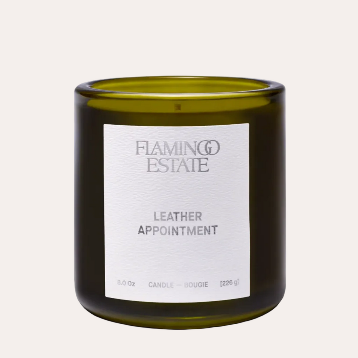 An 8.0 oz scented candle in an olive green glass jar with a white label reading 'FLAMINGO ESTATE LEATHER APPOINTMENT' on a light beige background.