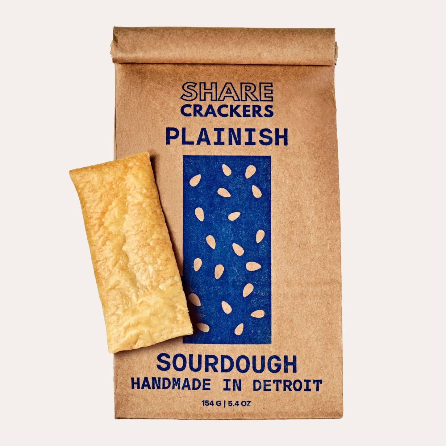 A kraft paper bag of Share Crackers Plainish Sourdough, with a single rectangular sourdough cracker leaning against the left side of the package, on a light beige background.