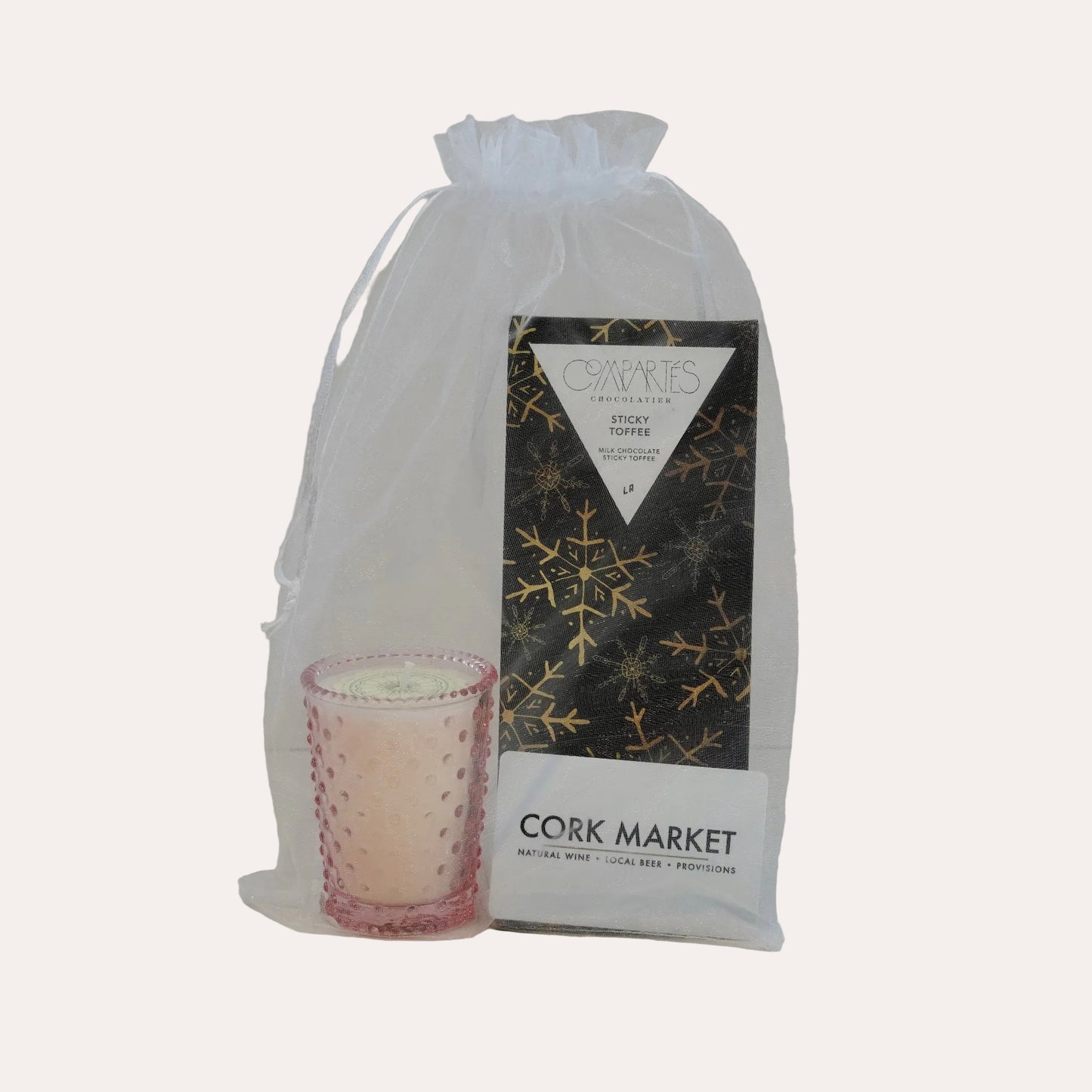 Candle in a pink holder with a white drawstring bag labeled 'Cork Market' on a light gray background